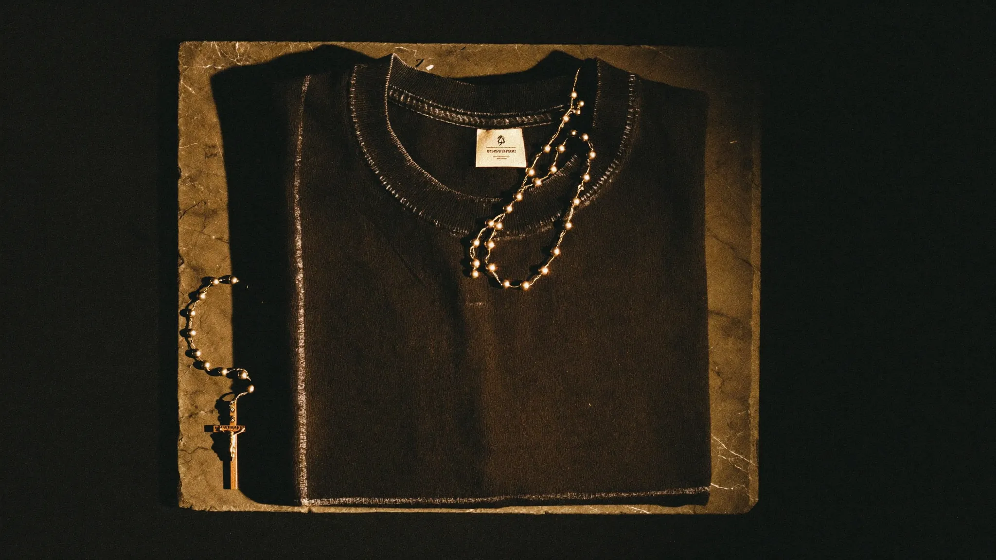 Crowned Choices tee folded on dark stone beside a rosary